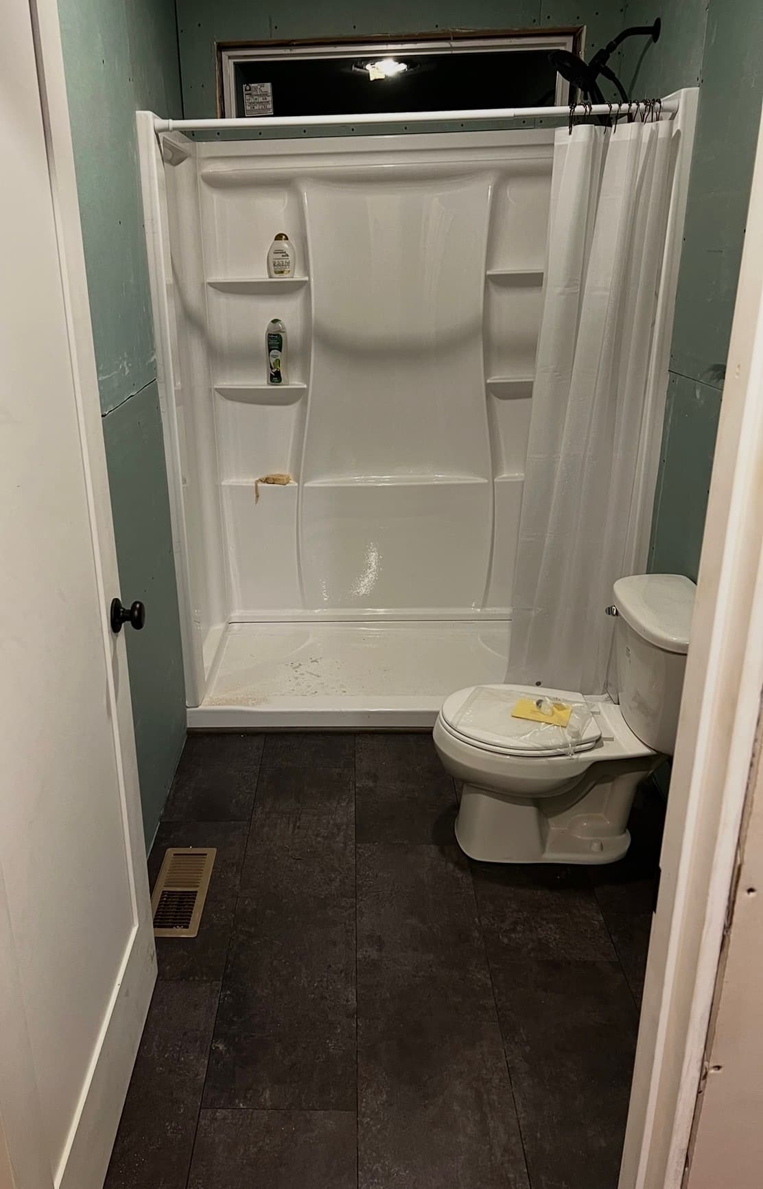 Renovated bathroom with new shower surround, toilet, and dark plank flooring
